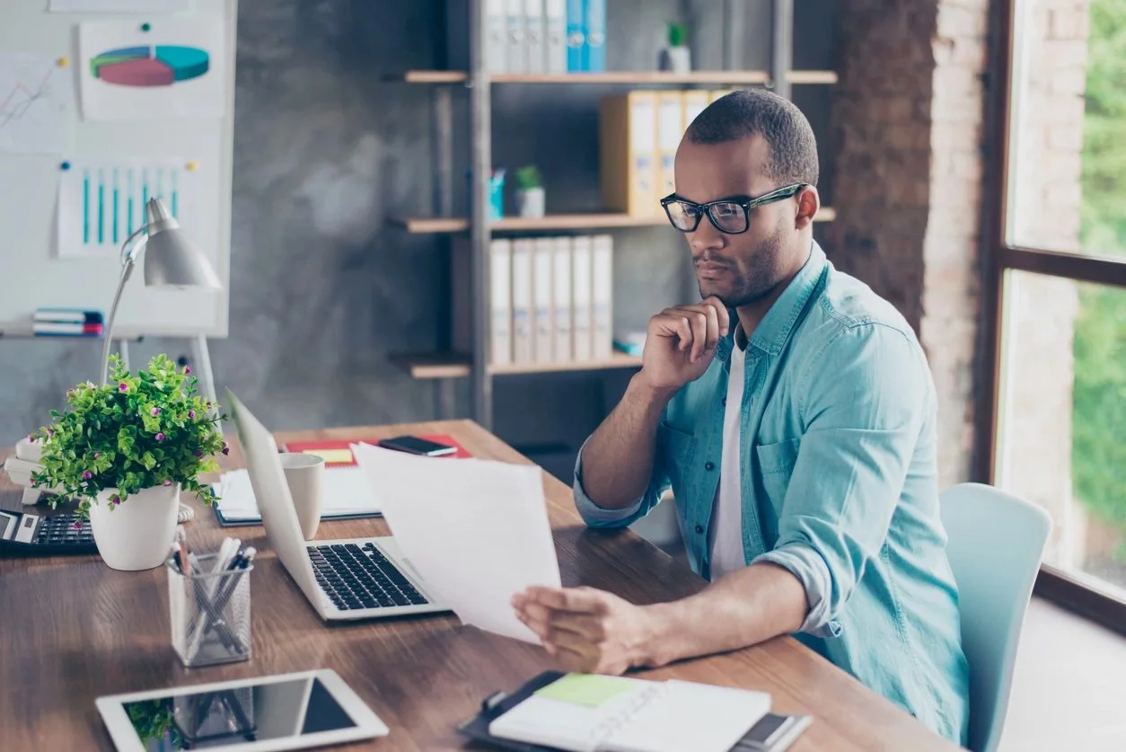 A man looking at a paper while sitting in front of a desk